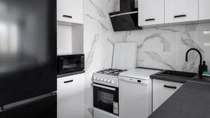 Una cocina moderna con armarios blancos, un refrigerador negro, una estufa a gas y un microondas.