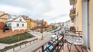 A balcony with a white wicker chair, overlooking a street with parked cars and colorful buildings. - Old Town 5-Bedroom Apartment (Warszawa)