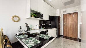 A modern kitchen with white cabinetry, a black countertop, and a wooden door. - Wola Chic Luxury Studio (Warszawa)