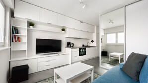 A modern living room with a flat-screen TV, white furniture, a small kitchen area, and a blue sofa. - Rakowiec Blue Studio (Warszawa)