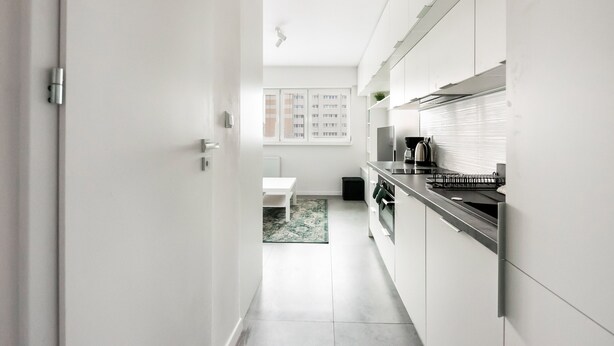 A modern kitchen with white cabinets, a black countertop, and a view of a residential building in the background. - Rakowiec Blue Studio (Warszawa)