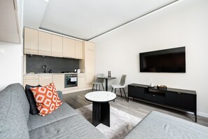 Un salon moderne avec un canapé gris, une table basse ronde et un téléviseur fixé au mur.