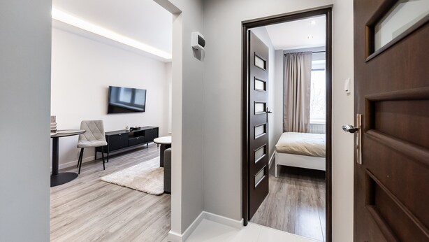 Un dormitorio moderno con cama, televisor montado en la pared, escritorio con silla y armario.