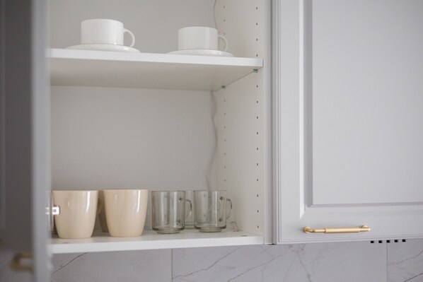 A kitchen with white cabinets, a marble backsplash, and a white shelf with cups and glasses.