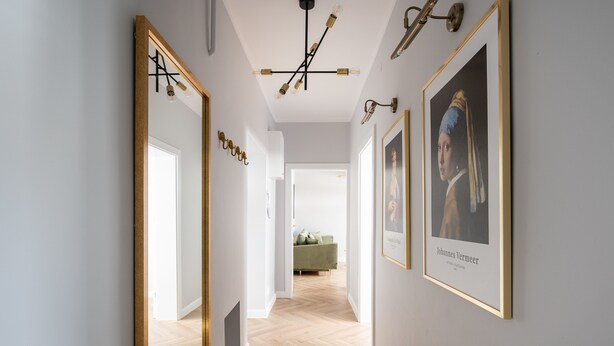 A hallway with a wooden floor, a black mat, and framed artwork on the walls.