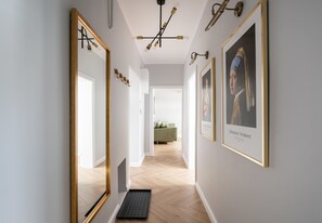 A hallway with a wooden floor, a black mat, and framed artwork on the walls.