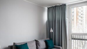Una sala de estar moderna con un sofá gris, cojines color turquesa, una lámpara de pie y un ventanal con cortinas grises.