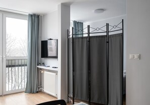A modern hotel room with a large window, a radiator, a flat-screen TV, and a curtain divider.