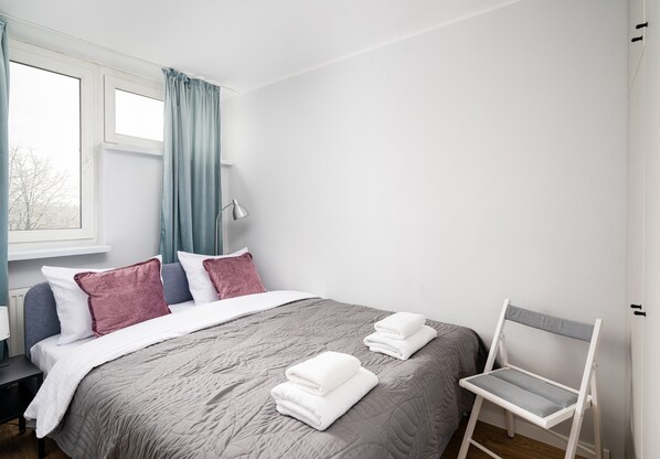 A neatly made bed with a grey quilt, two pillows, and folded white towels.