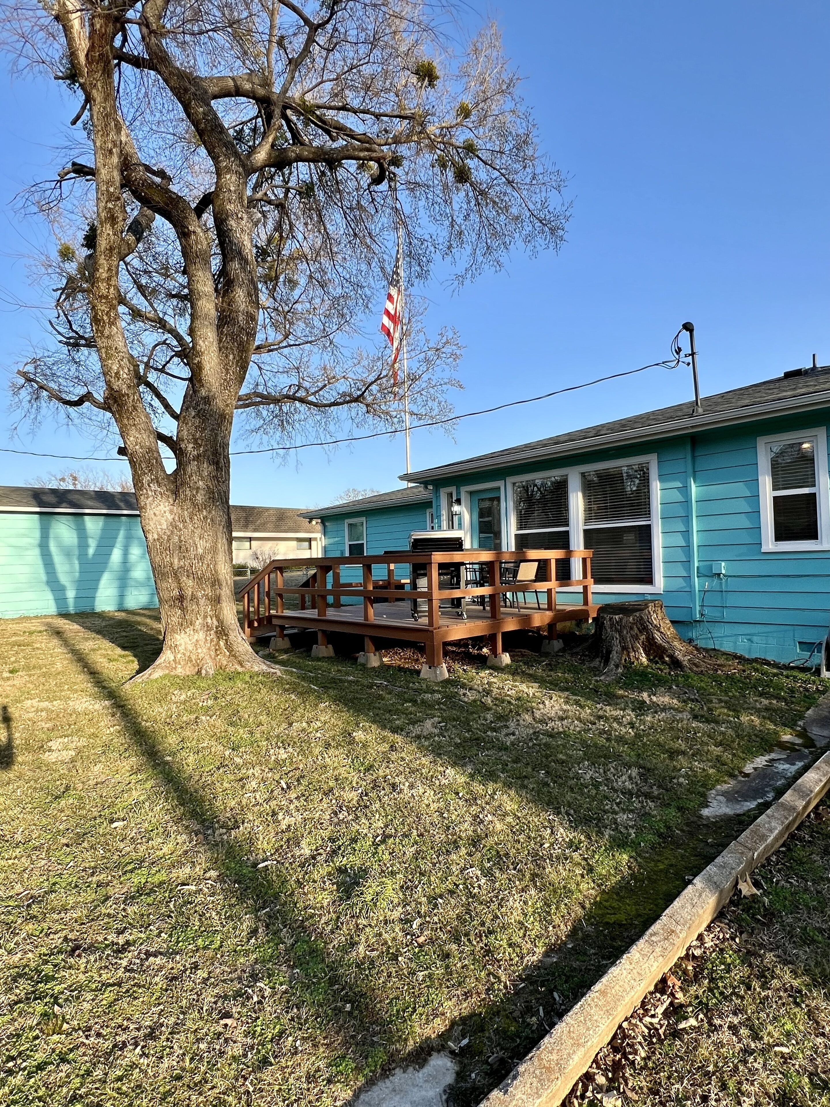 Ein blauer Wohnwagen mit einer Holzterrasse und einem großen Baum davor.