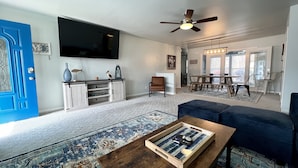 A spacious living room with a large TV, a ceiling fan, a dining area, and a blue door. - Home in Disney - Ride Directly to Trails, 1/2 mile to Marina & Boat Ramp (Disney)
