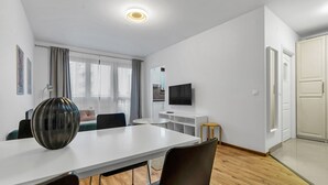 A modern, well-lit room with a dining table, chairs, a TV, and a kitchen area. - Metro Bemowo Comfort Studio (Warszawa)