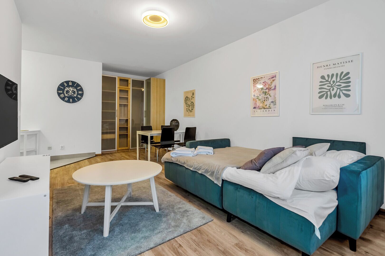 A modern, well-lit room with a teal sofa, a round table, and a wardrobe with sliding doors.