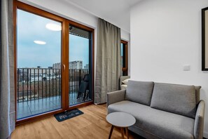 A modern living room with a grey sofa, a small round table, and a view of a cityscape through large sliding glass doors.