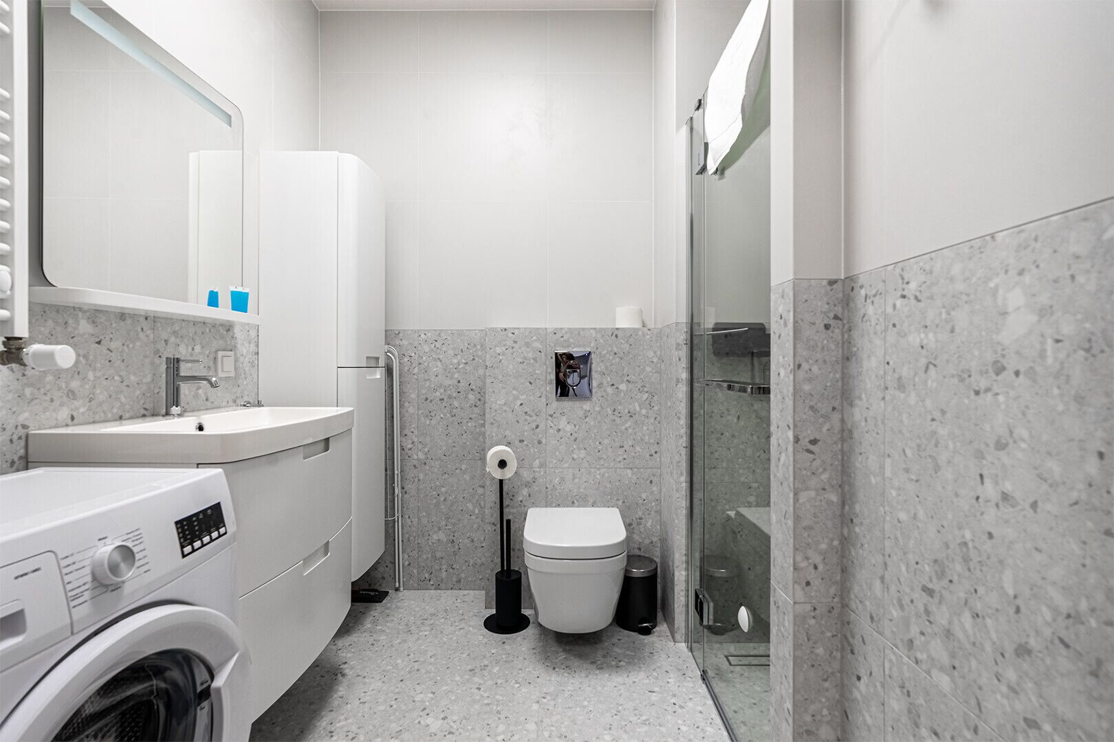 Ein modernes Badezimmer mit Waschmaschine, Waschbecken, Toilette und einer Duschkabine aus Glas.