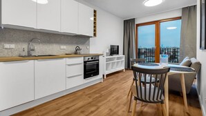 A modern kitchen with white cabinets, a wooden countertop, and a built-in oven. There is a dining area with a table and chairs, and a large window offering a city view. - Metro Wierzbno Cosy Apartment (Warszawa)