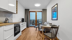 A modern kitchen with a kettle, stove, and dining area with chairs and a table. - Metro Wierzbno Cosy Apartment (Warszawa)