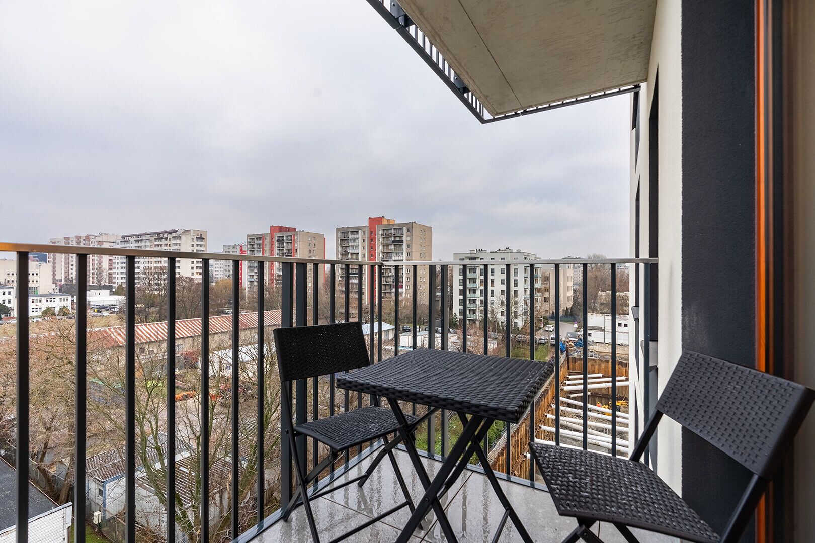 Un balcon avec une table et deux chaises, donnant sur un paysage urbain composé de nombreux immeubles.