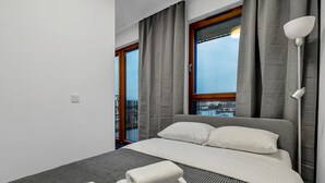A modern hotel room with a large bed, grey curtains, a view of the city, and a balcony. - Metro Wierzbno Cosy Apartment (Warszawa)