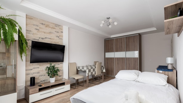 Ein modernes Schlafzimmer mit einem großen Bett, einem an einer Holzwand montierten Fernseher, einem Schreibtisch mit Stühlen und einem Kleiderschrank.