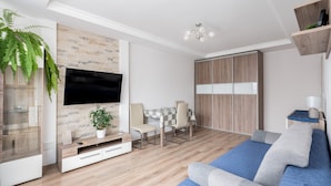 Ein modernes Wohnzimmer mit Fernseher, einem Esstisch mit Stühlen, einer Couch und einem Holzschrank.