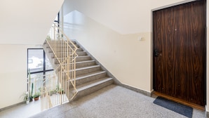 Eine Holztreppe mit Geländer führt zu einer oberen Etage, eine Holztür und Blumentöpfe in der Nähe eines Fensters.