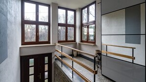Um quarto com pé direito alto, grandes janelas, um banco de madeira e uma parede de pedra.