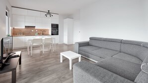 A modern living room with a grey sofa, a white coffee table, and a TV on a wooden table. - 10th Floor Unii Lubelskiej Apartment (Poznań)