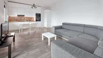 A modern living room with a grey sofa, a white coffee table, and a TV on a wooden table.