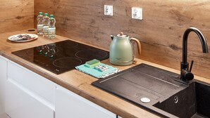 A modern kitchen with a wooden backsplash, a black induction cooktop, a kettle, and a sink with a faucet. - 10th Floor Unii Lubelskiej Apartment (Poznań)