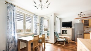 A modern kitchen with wooden cabinets, a refrigerator, and a dining area with a table and chairs. - Ceramiczna Comfort Studio (Warszawa)