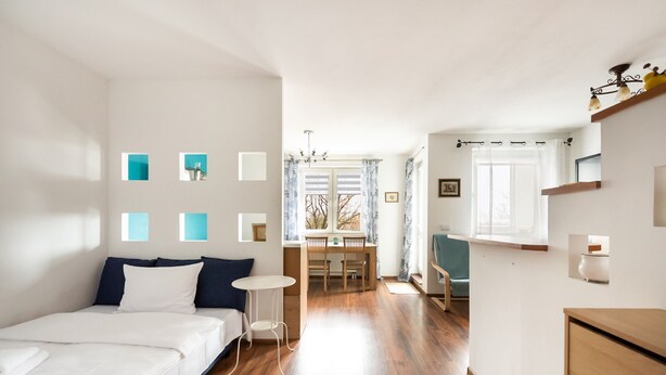 A bedroom with a bed, a small table, and a desk with a chair. There is a window with curtains and a view of the outside. - Ceramiczna Comfort Studio (Warszawa)