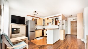 A modern kitchen with wooden cabinets, a built-in oven, and a large flat-screen TV. - Ceramiczna Comfort Studio (Warszawa)