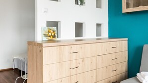 A modern room with a wooden dresser, a grey sofa, and a teal accent wall. - Ceramiczna Comfort Studio (Warszawa)