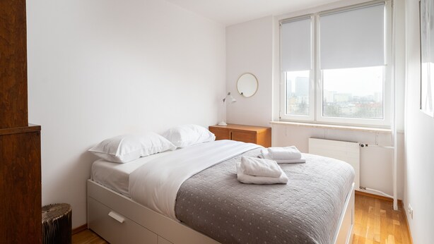 Un dormitorio con una cama, mesita de noche, espejo y ventana con persianas.
