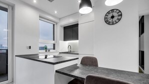 Een moderne keuken met een centraal eiland, een eethoek met een tafel en stoelen, en een grote wandklok.