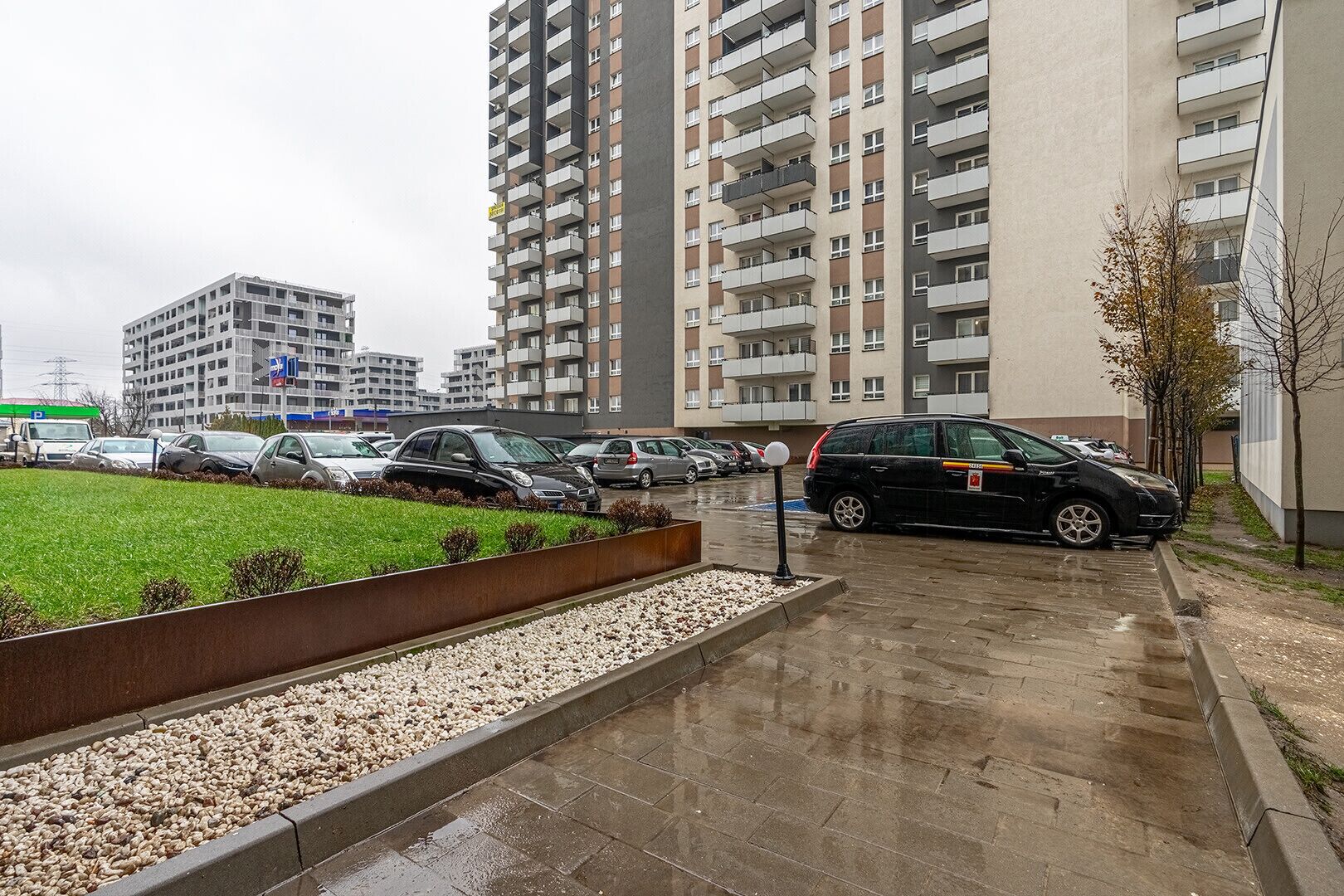 A parking area with multiple cars, a grassy area, and a building with balconies.