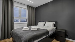 Een moderne slaapkamer met een groot bed, grijze gordijnen, uitzicht op de stad en een nachtkastje.