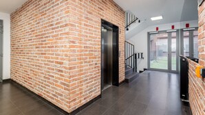 A modern interior with a brick wall, a black elevator, and a glass door leading outside. - Cracow Novum Apartment #58 (Kraków)