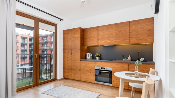A modern kitchen with wooden cabinets, a built-in oven, and a dining area with a table and chairs. - Cracow Novum Apartment #58 (Kraków)