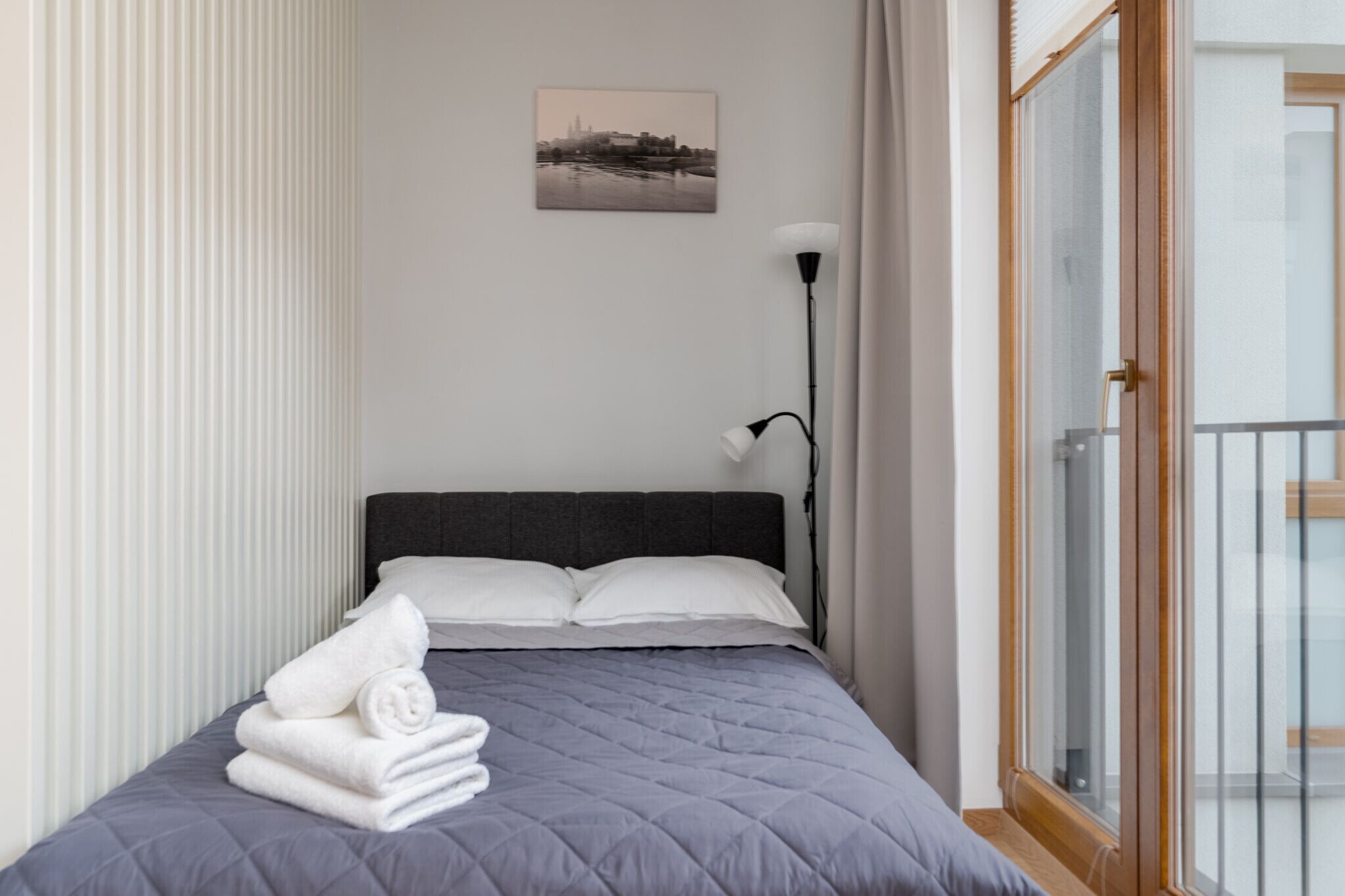 Un lit bien fait, avec une couverture grise, des oreillers blancs et des serviettes pliées posées sur le bord.