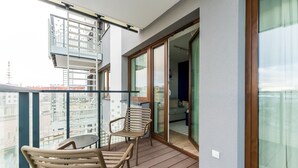 Varanda com duas cadeiras, uma mesa e portas de correr de vidro, com vista para a paisagem urbana.