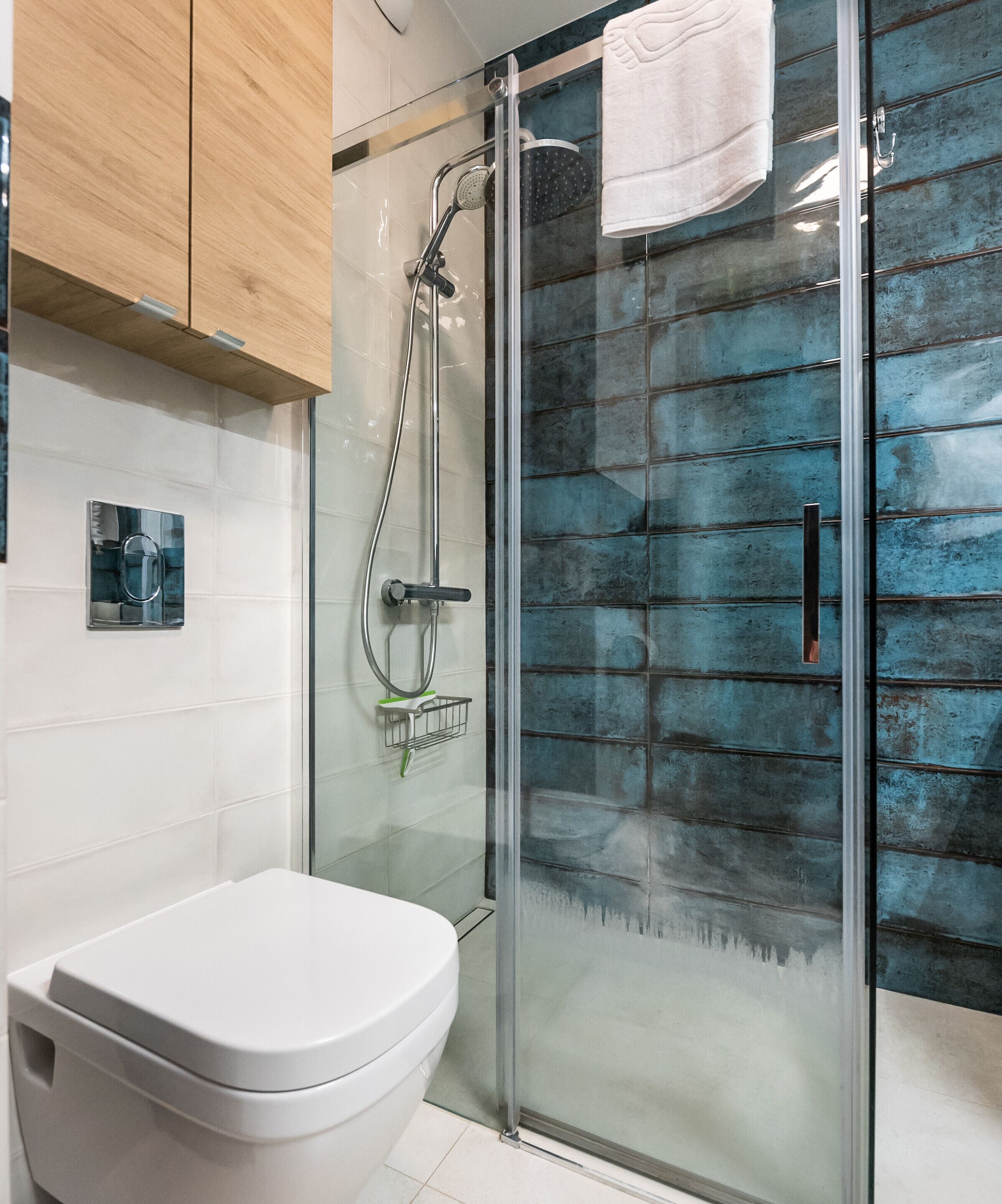 A modern bathroom with a glass shower enclosure, a white toilet, and a blue-tiled wall.
