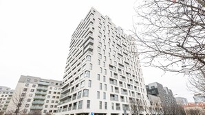 En høj, moderne lejlighedsejerforening med flere altaner og en DHL-leveringsvogn parkeret foran.