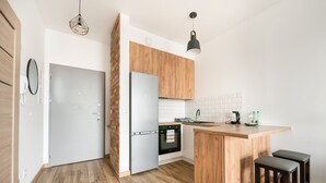A modern kitchen with wooden cabinets, a built-in oven, a refrigerator, a sink, and two stools.