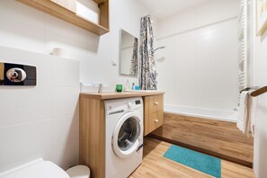 Une salle de bain moderne équipée d’un lave-linge, de toilettes et d’un espace douche.