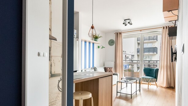 A modern kitchen with a wooden countertop, a bar stool, and a dining area with a table and chairs. - Daniszewska Cosy Apartment (Warszawa)