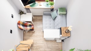 A compact living space with a sofa, a small table with a vase of flowers, a desk with a computer, and a staircase leading to another level. - Piotrkowska Studio with Mezzanine (Lódz)