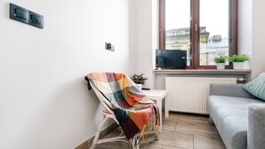A modern living room with a wicker chair, a grey sofa, a television on a wooden shelf, and a window with a view of buildings. - Piotrkowska Studio with Mezzanine (Lódz)