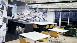 A modern office space with a central island table, yellow chairs, and a green sofa.